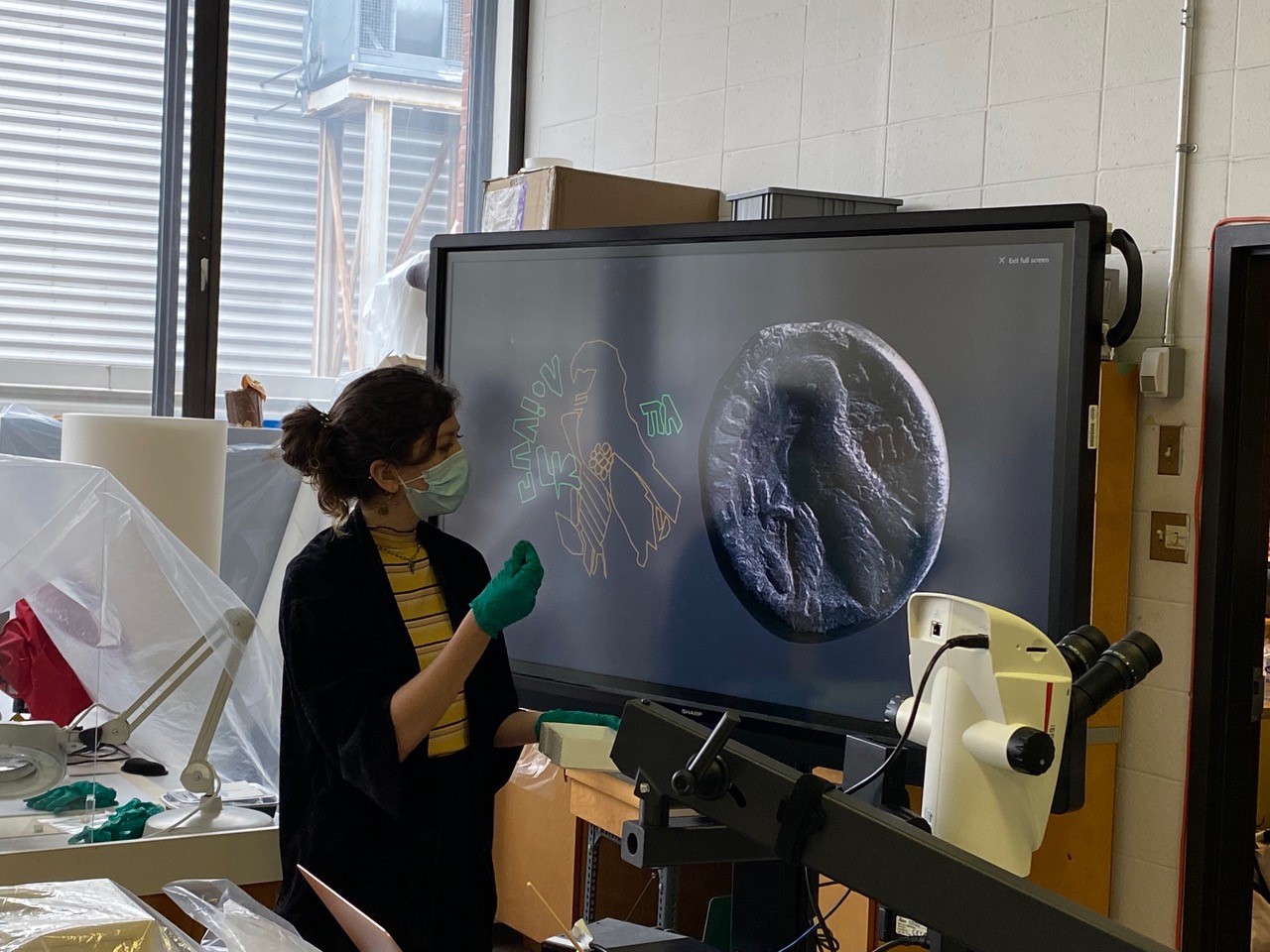 photo of Prof Emy Kim looking at screen showing an ancient coins from the Diniacopoulos Collection