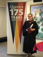 A graduate on the right of a 175th anniversary of Queen's University banner