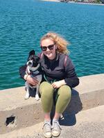 Photograph of Meghan Greavette sitting next to the water, with a dog.