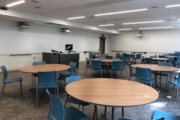 Classroom with large round tables and blue chairs. 