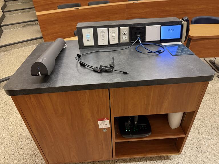 Top down view of the podium. The podium has a document camera, lecture capture, display cables, and a set of microphones. The podium is not height adjustable, but is accessible.