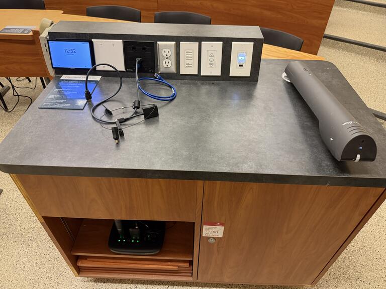 Top down view of the podium. The podium has a document camera, lecture capture, display cables, and a set of microphones. The podium is not height adjustable, but is accessible.