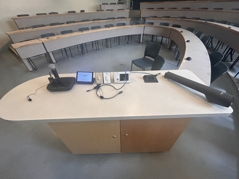Top-down view of podium. Microphones on the left; touch panel control system and light switches at center; document camera on the right.