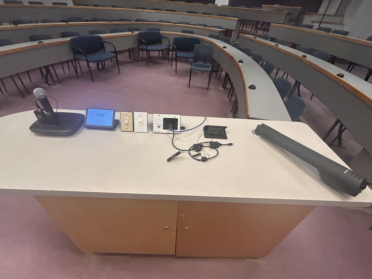 Top-down view of podium. Microphones on the left; touch panel control system and light switches at center; document camera on the right.