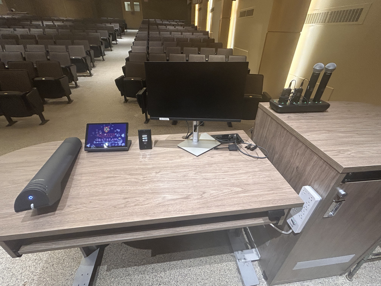 Top-down view of podium. Document camera on the left; touch panel control system and monitor at center; microphones on the right.