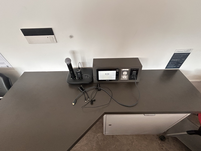 Top-down view of podium. A set of microphones on the left; touch panel control system and connection outlet on the right.