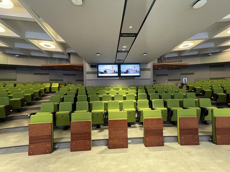 View of the classroom from the instructor’s podium. Rows of seating are tiered, and each seat had a tablet arm. The entryway door is located at the rear of the room. This classroom is accessible for instructors.