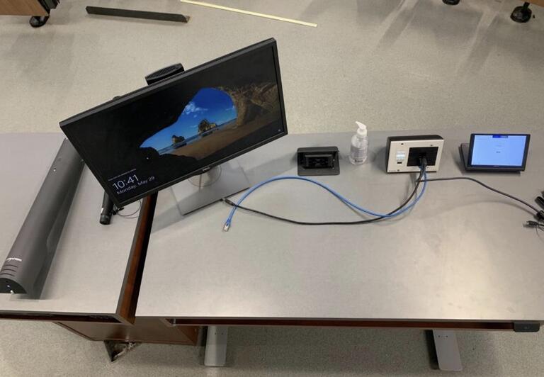 Top-down view of the instructor’s podium. The podium is equipped with a monitor, a document camera, and microphones. The podium is height adjustable and accessible for instructors. 