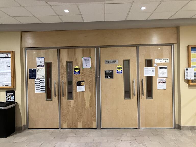 Entryway door to Biosciences complex, room 1102. There are two sets of double doors with handles that pull to open. Both doors can be opened by pressing the automatic door opener beside the entrance. 