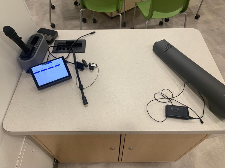 Top-down view of the instructor’s podium. The podium is equipped with a set of microphones and connection cords to project media and a document camera.