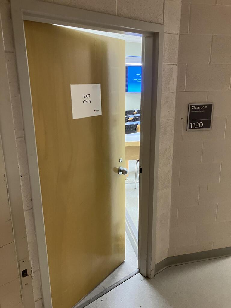 Door to Biosciences room 1120 and a wooden door and has a doorknob on the right side. 