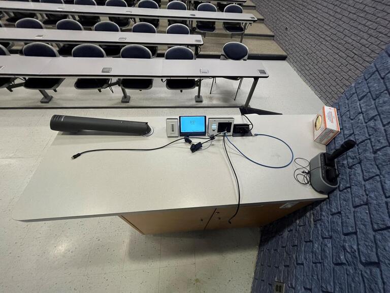 Top down view of the podium. The podium is equipped with a set of microphones, a document camera, lecture capture, and wireless presentation. This podium is not height adjustable.