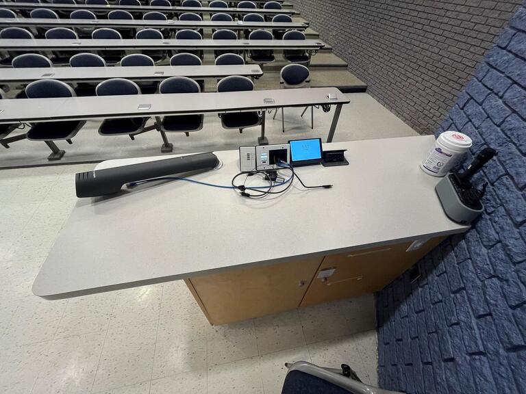 Top down view of the podium. The podium is equipped with a document camera, lecture capture, and a set of microphones. The podium is not height adjustable.