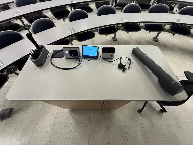 Top down view of the podium. The podium has a document camera, lecture capture, a set of microphones, and a display cable.