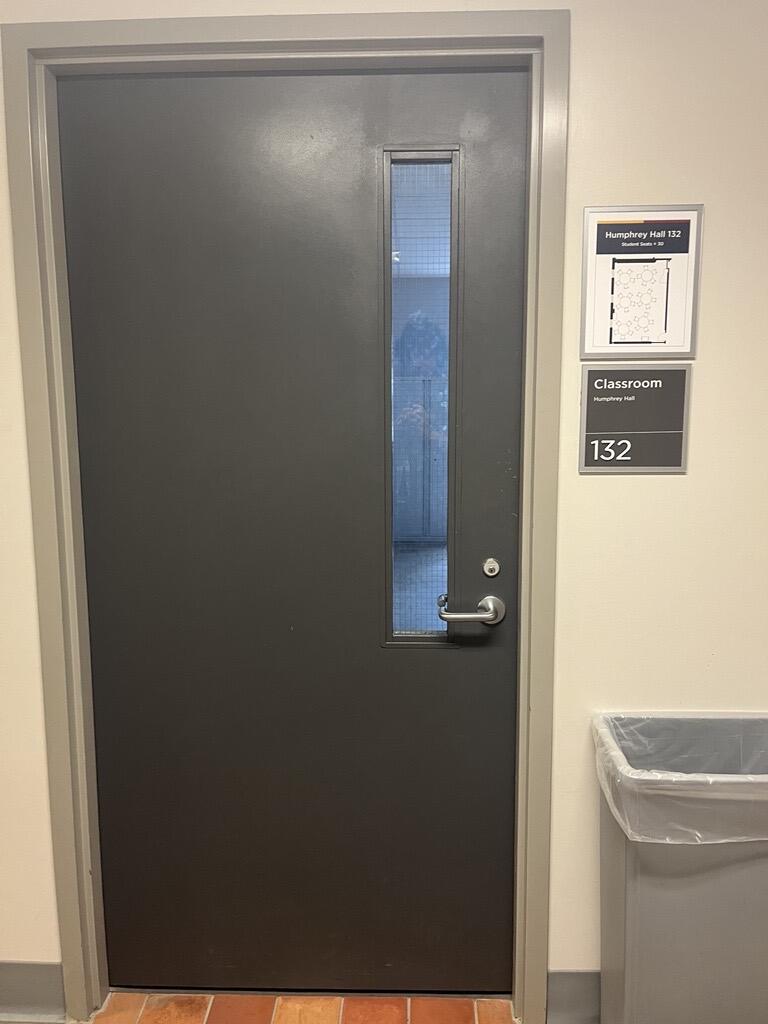 The entryway of room 132 in Humphrey Hall is a single grey door with a silver handle on the right side of the door. 