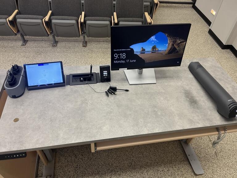 Top down view of the podium. Podium is equipped with a document camera, a computer, lecture capture and a set of microphones. The podium is height adjustable and accessible for instructors.