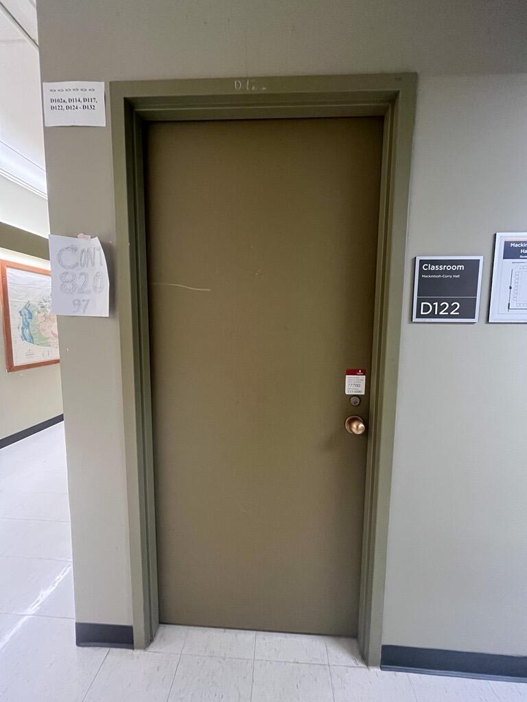The entryway of room D122 in Mackintosh Corry Hall is a brown door with a doorknob on the right side.