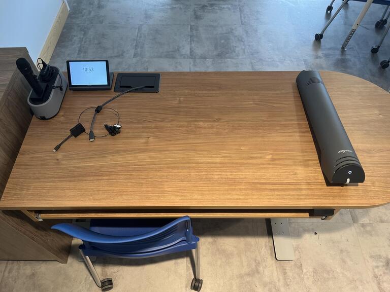 Top-down view of the podium. The podium has a set of microphones, document camera, and set of display cables. The podium is height adjustable and accessible.