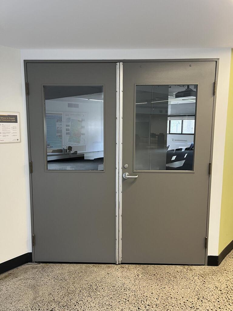 The entryway door of room D214 in Mackintosh Corry Hall is a double grey door with a lever handle on the right door.