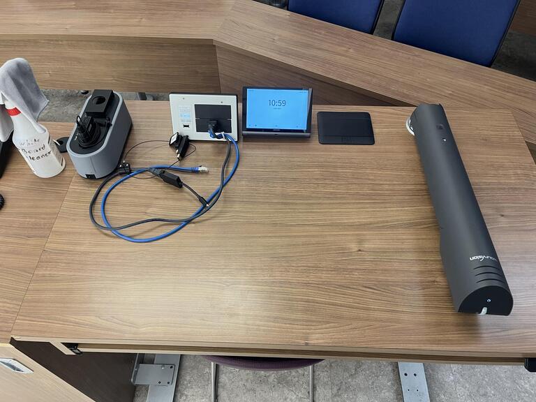 Top-down view of the podium in room D214 in Mackintosh-Corry Hall. The podium is equipped with a set of microphones, display cables, and a document camera.