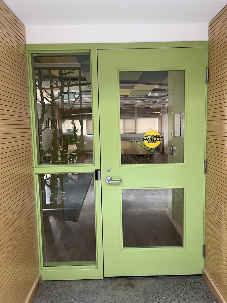 Door to enter room E202 in Mackintosh-Corry Hall. The door is green with a lever on the left side. There is an automatic operator.