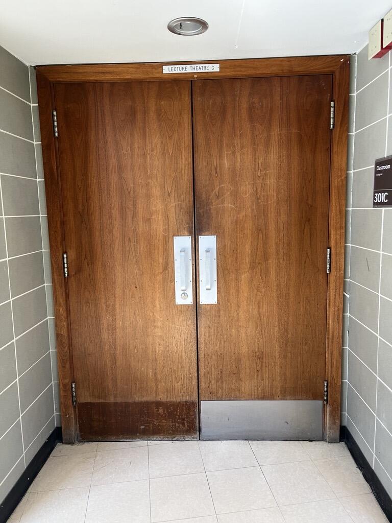 The entryway to room 301C in Stirling Hall. The double door has pull handles in the middle. There is no automatic operator.