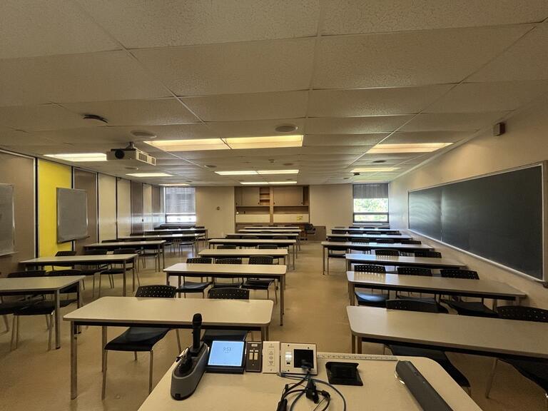View of the classroom from the instructor’s podium. There are six rows of long table and chairs for students. This classroom is accessible for instructors.