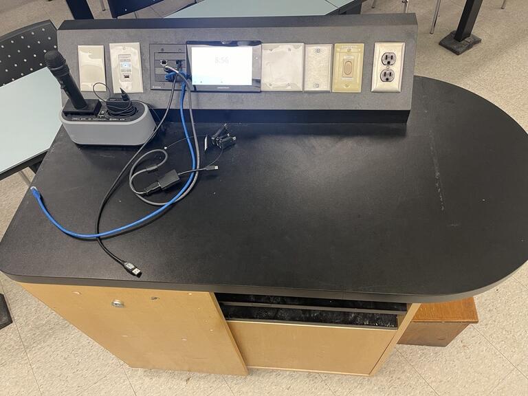 Top down view of the podium. Podium is equipped with lecture capture, an outlet and a set of microphones.