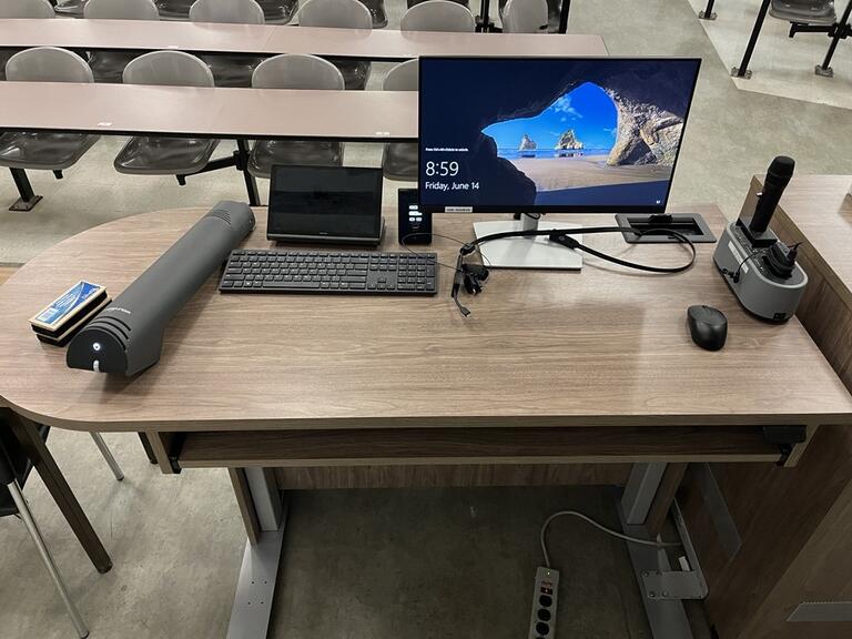 Top down view of the podium. The podium has a document camera, room PC, a set of microphones, and display cables. The podium is height adjustable and accessible.