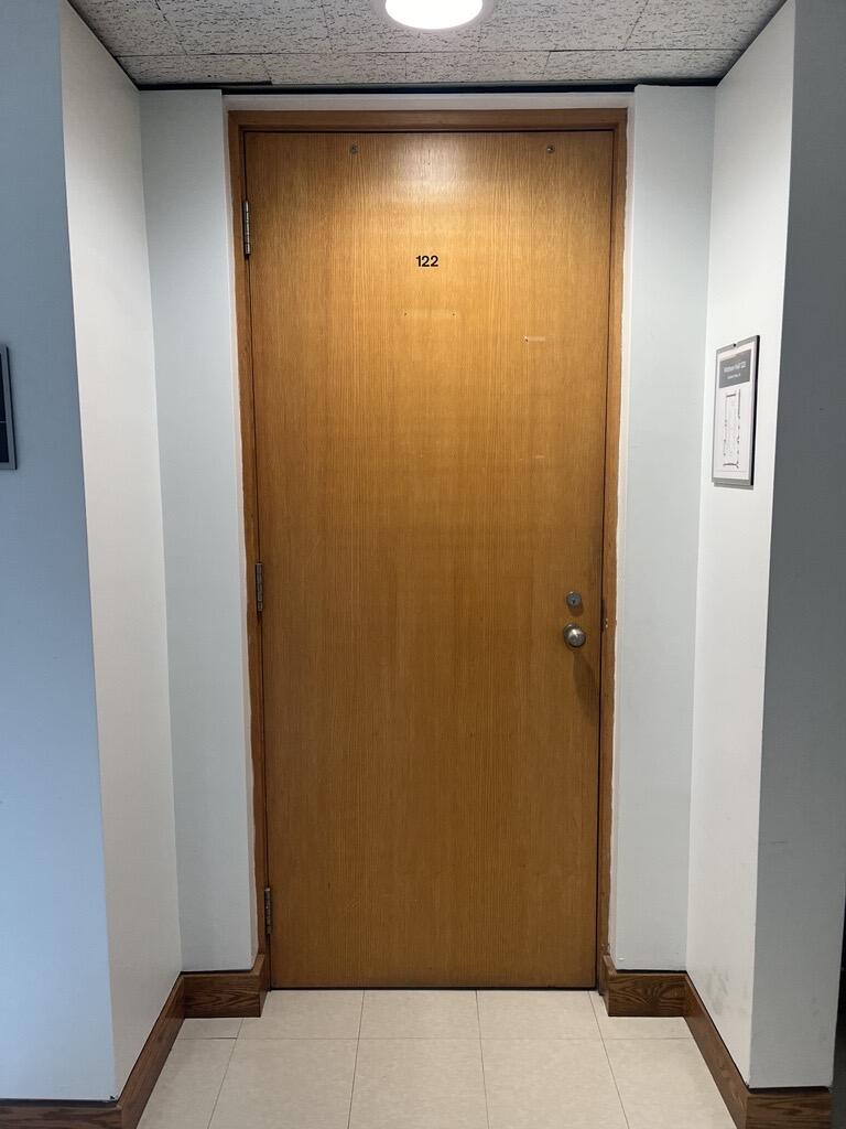 The entryway of room 122 in Watson Hall is a wooden door with a doorknob on the right side.