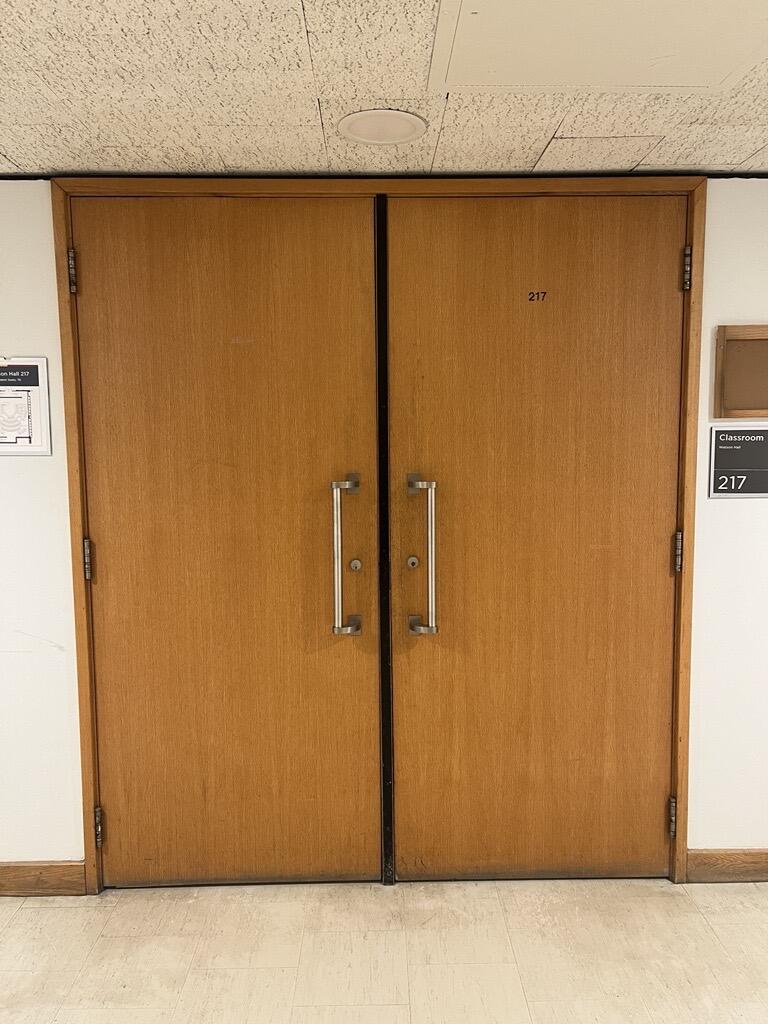 The entryway of room 217 in Watson Hall is a wooden double door with silver handles on each door.