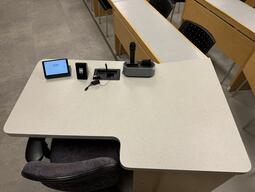 Top down view of the podium. The podium is equipped with a set of microphones, lecture capture, and wireless presentation. This podium is accessible for instructors.