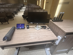 Top-down view of podium. Document camera on the left; touch panel control system and monitor at center; microphones on the right.