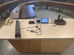 Top-down view of podium. Telephone and document camera on the left; touch panel control system and light switches at center; microphones on the right.