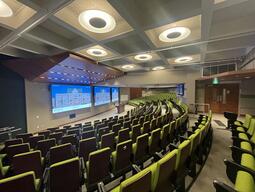 View of the classroom from a student seat at the rear of the room. Instructor’s podium is located at the front of the room. A whiteboard is located on the right wall, close to the instructor’s podium. There are three video walls at the front of the room. 