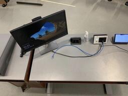 Top-down view of the instructor’s podium. The podium is equipped with a monitor, a document camera, and microphones. The podium is height adjustable and accessible for instructors. 