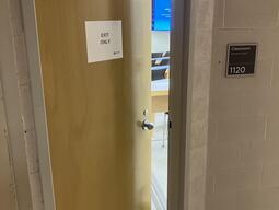 Door to Biosciences room 1120 and a wooden door and has a doorknob on the right side. 
