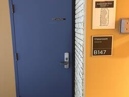 Image of the doors that enter Botterell Hall Room B147. The door has a metal handle on the right side. The door does not have automatic control.