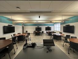 Instructors view while in the room, there are circular tables with 6 chairs each. The chairs are rolling chairs. There are ten (10) screens throughout the room to present media.