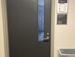 The entryway of room 132 in Humphrey Hall is a single grey door with a silver handle on the right side of the door. 