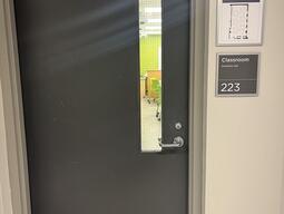Image of the door to enter Humphrey Hall room 223. The door is grey with a lever on the right side.