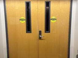 The entryway of the Auditorium in Humphrey Hall is a double door with a silver doorknob on the right door. There is an automatic door operator on the right of the doors.