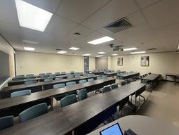 View of the classroom from the instructor’s podium. There are five rows of tables with chairs for students. The entryway door is located at the back of the room, on the right side. This classroom is not accessible for instructors.