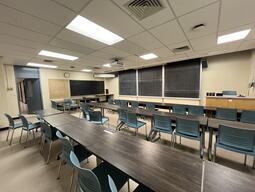 The podium is visible at the front of the room. This is the student’s point of view while sitting in the room. There are blackboards across the front of the room as well as a projector screen that can be pulled down while presenting.