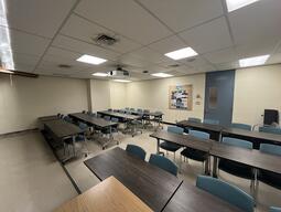 View of the classroom from the instructor’s podium. There are four rows of tables with chairs for students. The entryway door is located at the back of the room, on the right side. This classroom is not accessible for instructors.