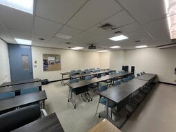 View of the classroom from the instructor’s podium. There are four rows of tables with chairs for students. The entryway door is located at the back of the room, on the left side. This classroom is not accessible for instructors.