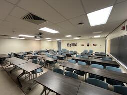 View of the classroom from the instructor’s podium. There are rows of tables with chairs for students. The entryway door is located at the back of the room, on the left side. This classroom is not accessible for instructors.