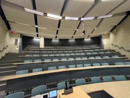 View of the classroom from the instructor’s podium. There are seven rows of long, curved tables with chairs for students. This classroom is not accessible for instructors.