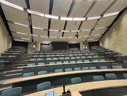 View of the classroom from the instructor’s podium. There are eight rows of long, curved tables with chairs for students. This classroom is not accessible for instructors.