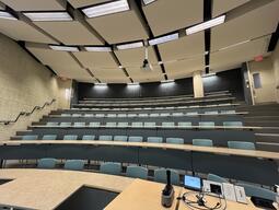 View of the classroom from the instructor’s podium. There are eight rows of long, curved tables with chairs for students. This classroom is not accessible for instructors.